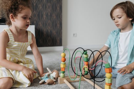 Kids engaging with colorful bead maze toy on carpet, promoting cognitive skills.