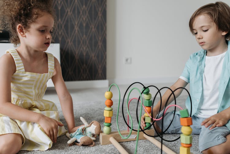 A Girl And Boy Sitting On The Carpet While Playing Toys