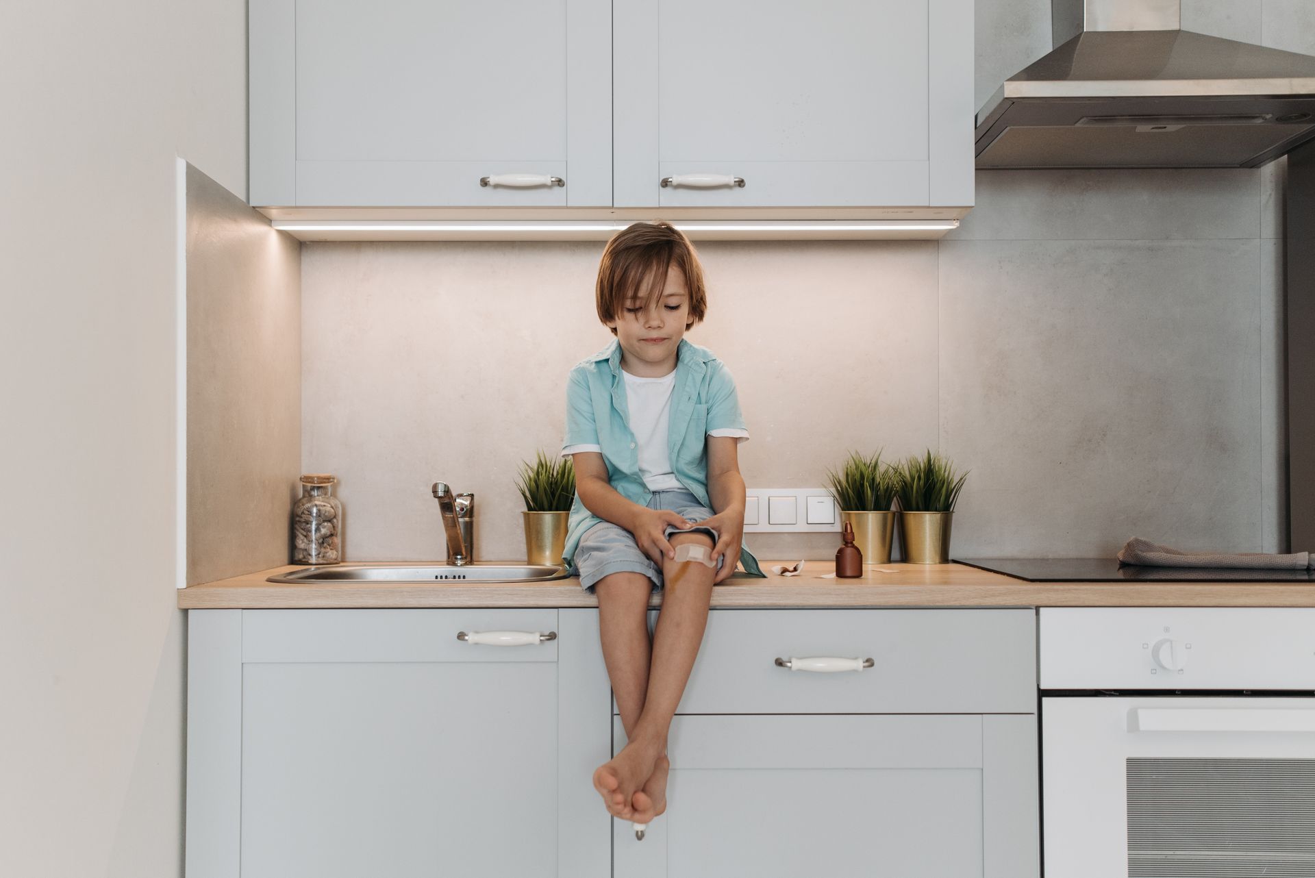 Little Boy with a Plaster on His Knee Sitting on a Kitchen Counter