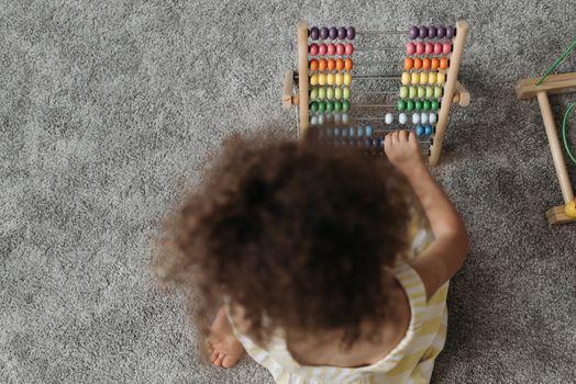 Photo by Pavel Danilyuk A young girl engaging with a colorful wooden abacus on a carpet, showcasing playful learning.