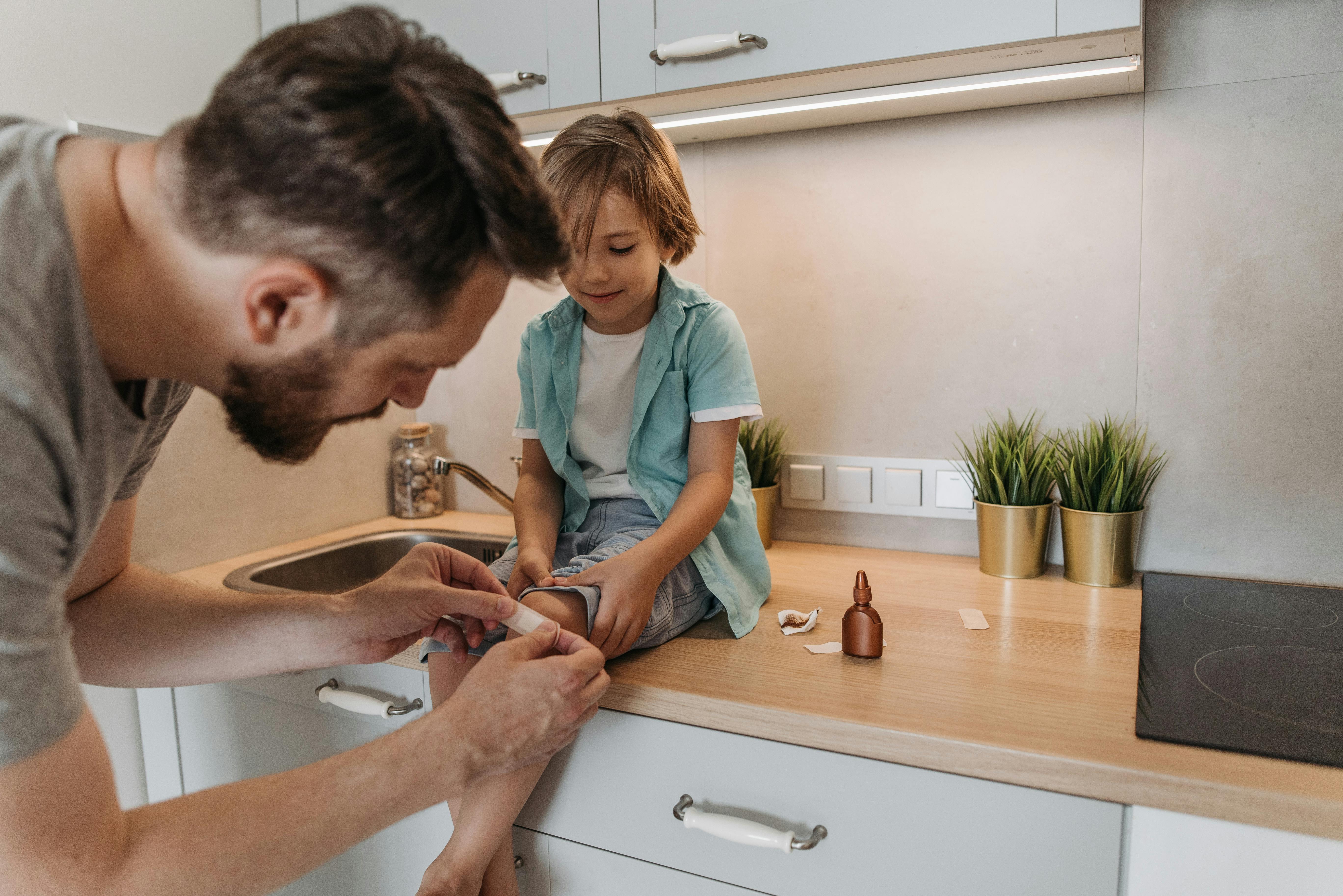 A father bandaging his child's knee on a kitchen counter, showcasing parental care.