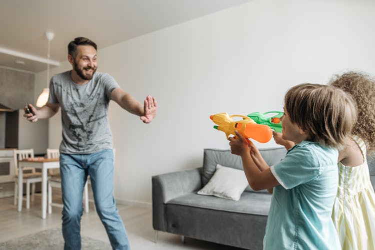 A Young Kids Pointing Water Guns To Their Father In Gray Shirt