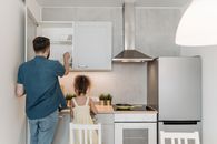 A Man Standing Beside a Little Girl Getting Plates From the Wooden Cabinet of the Kitchen