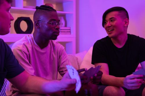 Free A group of diverse friends playing cards and enjoying a fun night indoors with mood lighting. Stock Photo