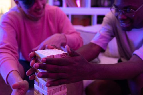 Free Two friends enjoying a game of Jenga indoors with warm lighting, creating a cozy atmosphere. Stock Photo