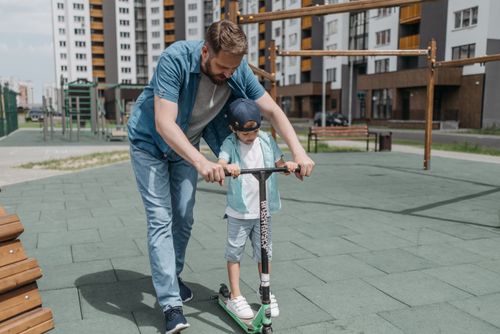 Free A father and son enjoy learning to ride a scooter together outdoors. Stock Photo