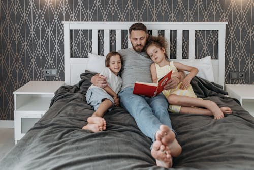Free A Man Reading a Book to His Children in Bed Stock Photo