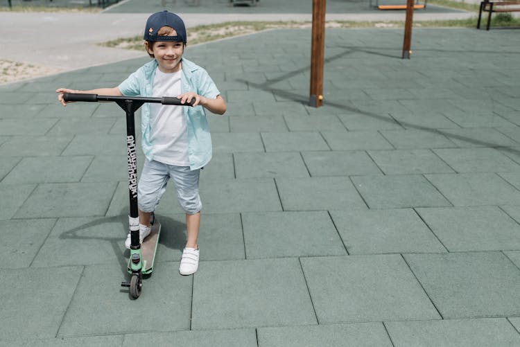 A Boy In White T-shirt And  Denim Shorts Riding A Scooter