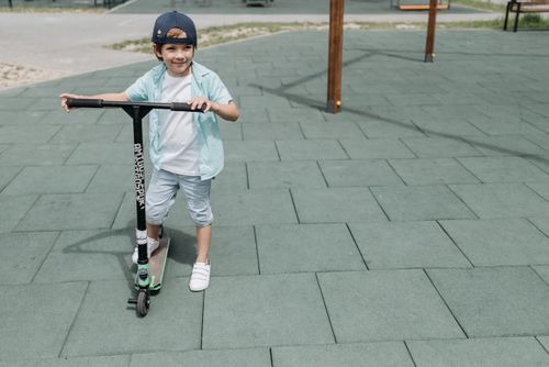 Free Child having fun riding a scooter at the park on a sunny day, showcasing joy and playfulness. Stock Photo