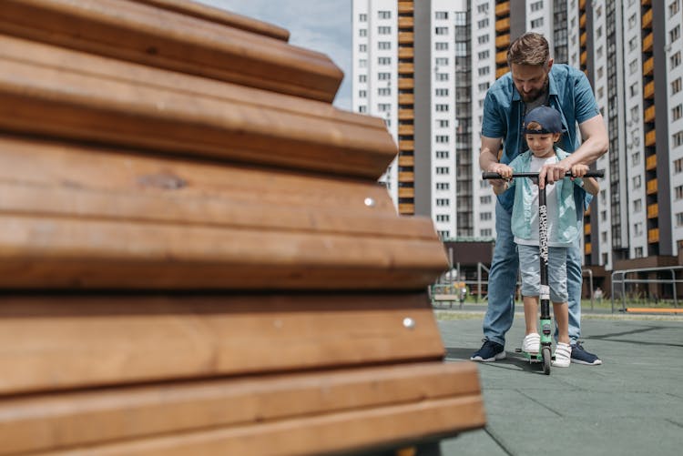 Man Teaching A Boy On How To Ride Scooter