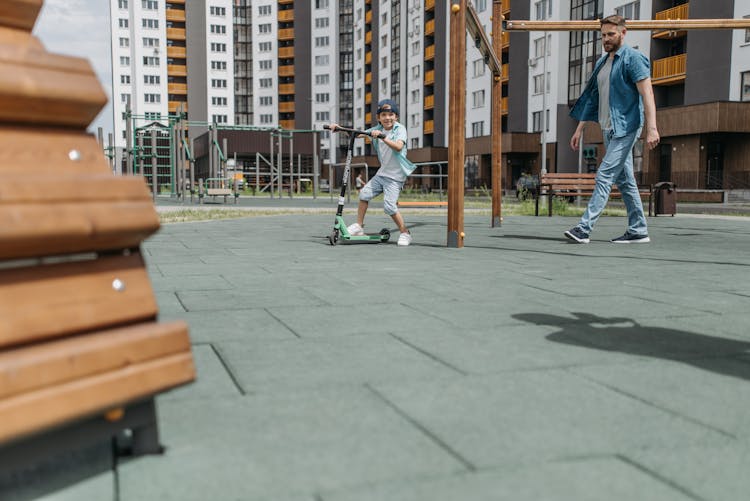 A Boy Riding A Scooter In The Park With His Father