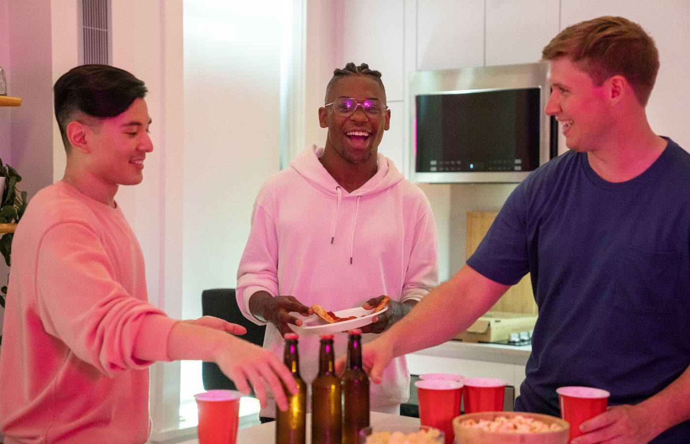 Group of friends laughing and enjoying pizza and drinks in a cozy kitchen setting.