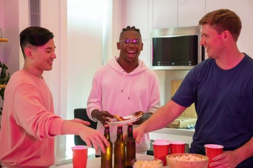 Free Group of friends laughing and enjoying pizza and drinks in a cozy kitchen setting. Stock Photo