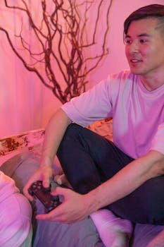 Young Asian man playing video games with a wireless controller indoors.