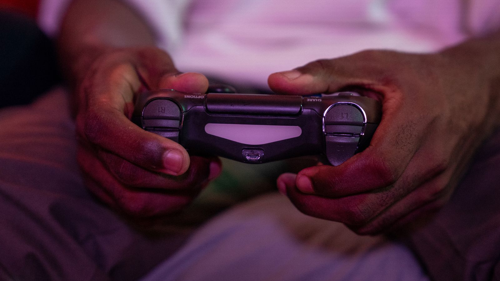 A person playing a game with a controller under coloured lighting