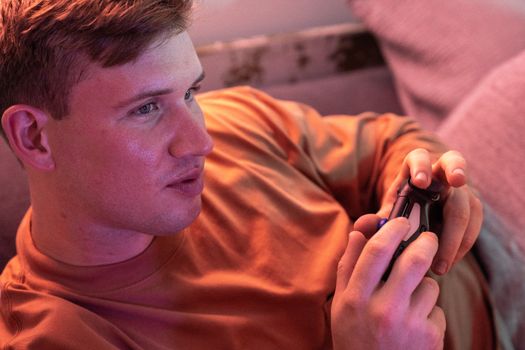 A young man plays video games on a comfortable couch, fully immersed in the experience.