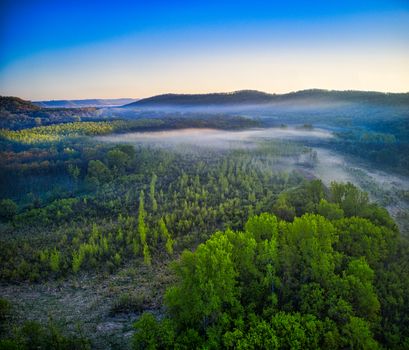 Aerial view of a mist-covered valley in Kellogg, Minnesota, showcasing lush green landscapes with a dramatic sky.