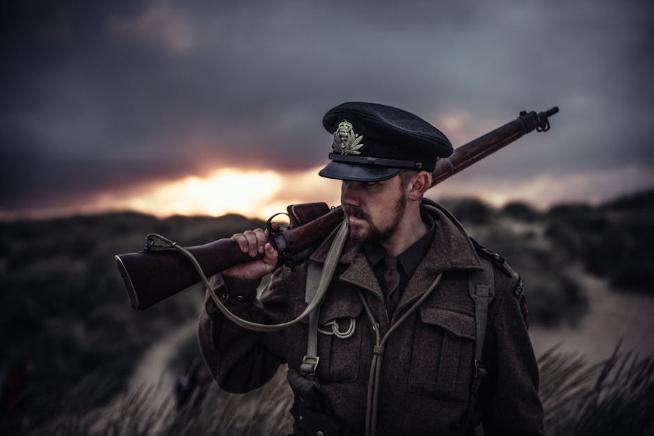 A soldier in uniform holding a rifle against a dramatic sunset background.