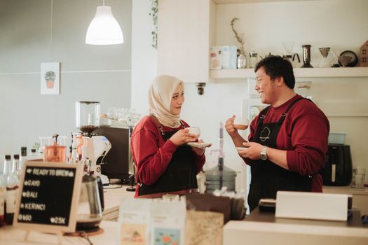 Two baristas sharing a fun coffee break inside a cozy café with warm lighting.