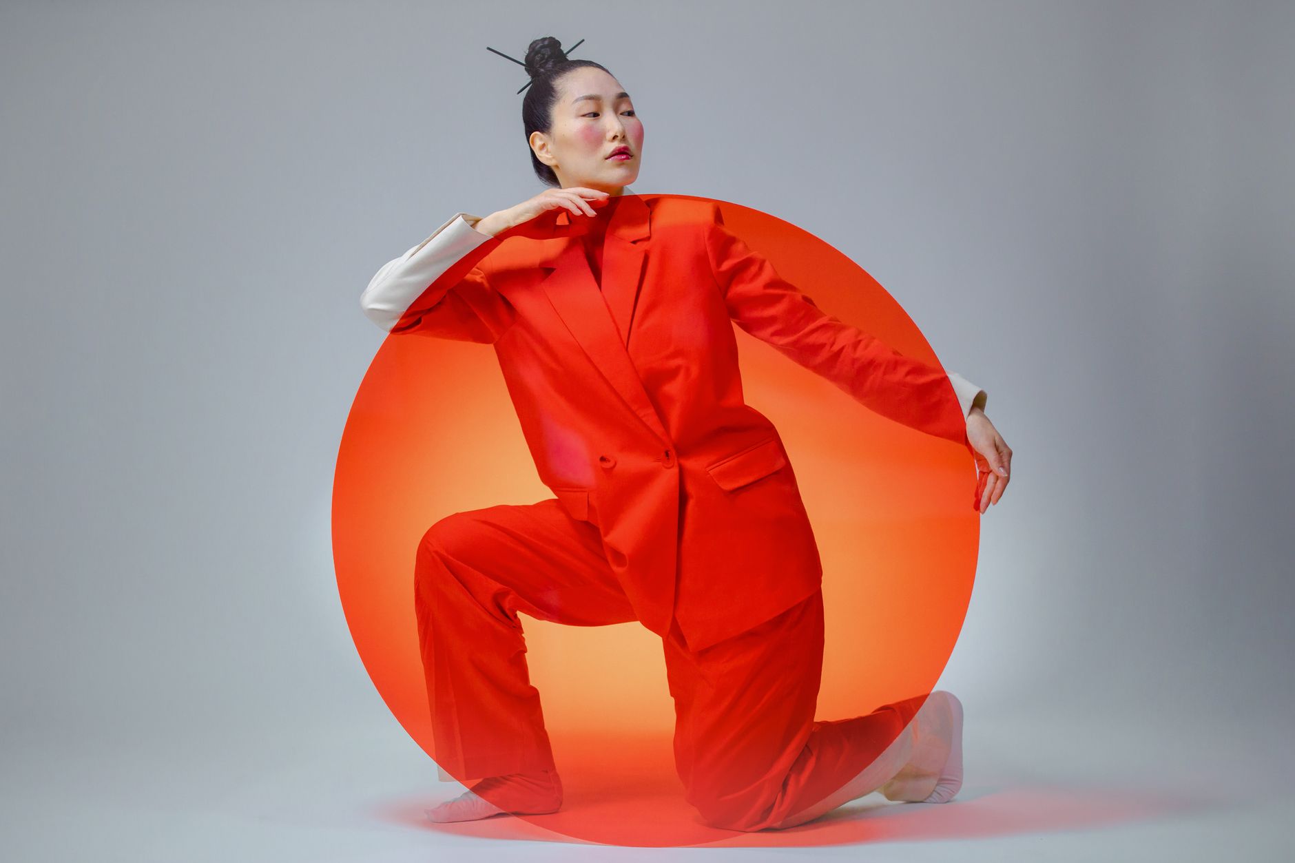 Vibrant and artistic portrait of an Asian woman posing in a bright red suit and a round panel in a studio setting.