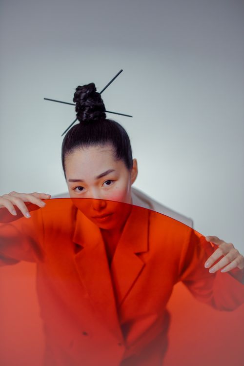Free Striking portrait of a woman with a hair bun holding a red glass in a studio setting. Stock Photo