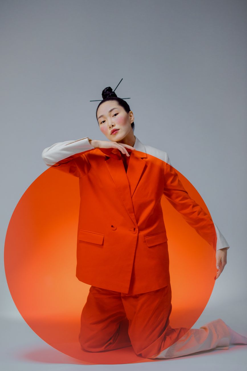 Model in vibrant orange attire with Japanese influences against a light grey backdrop.