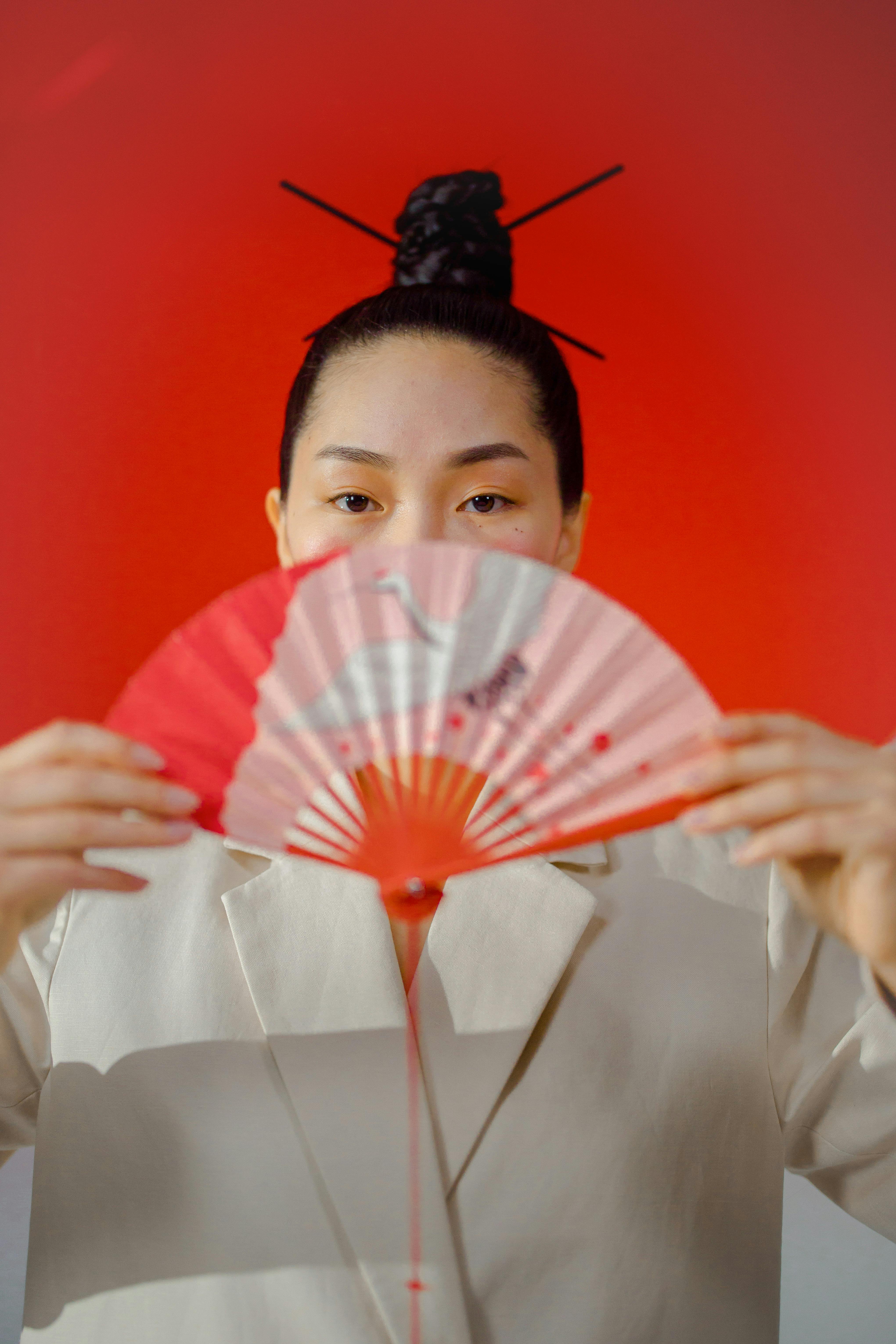 woman in white blazer holding pink and red hand fan