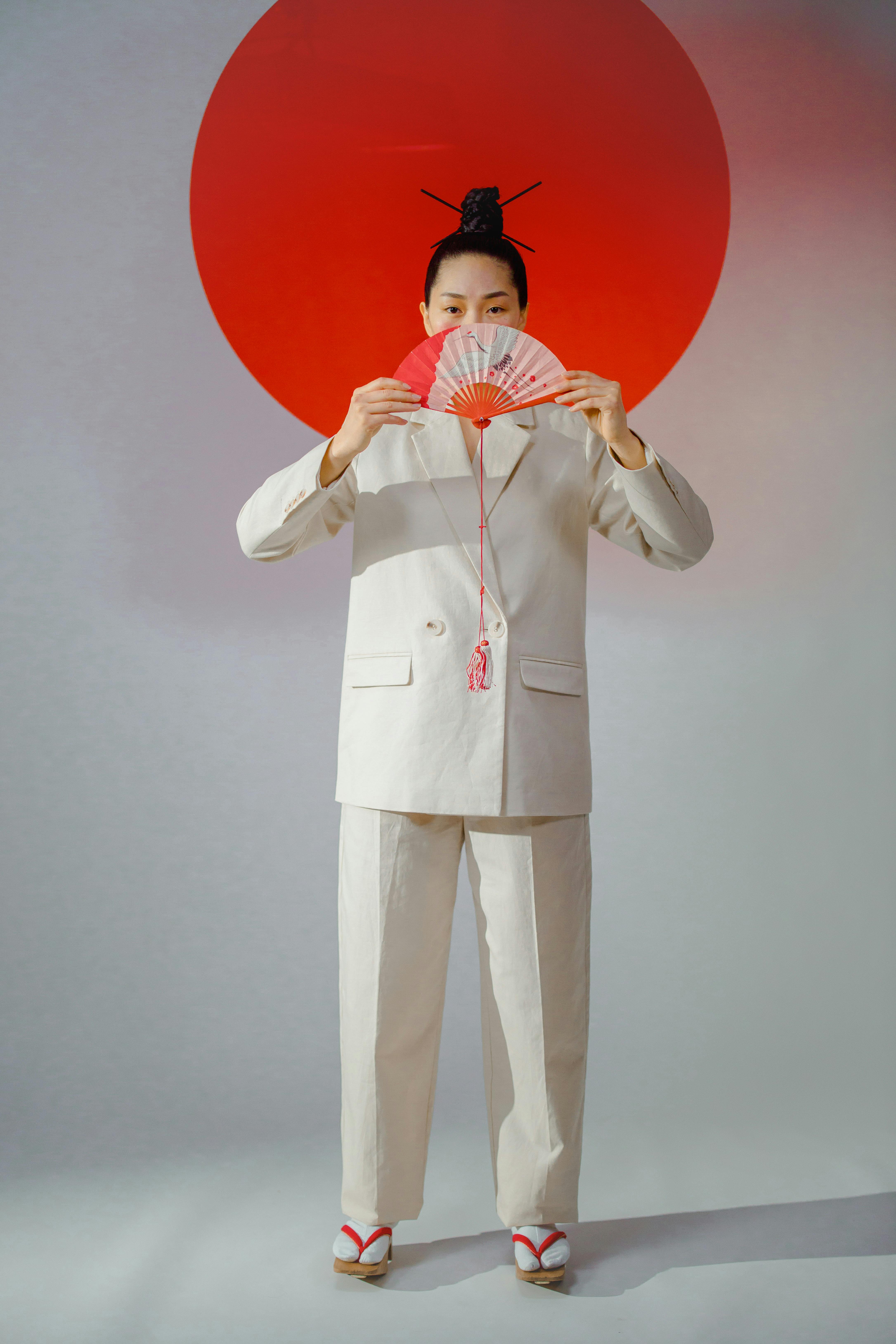 a woman in white suite holding a han fan while standing near the backdrop with red circle