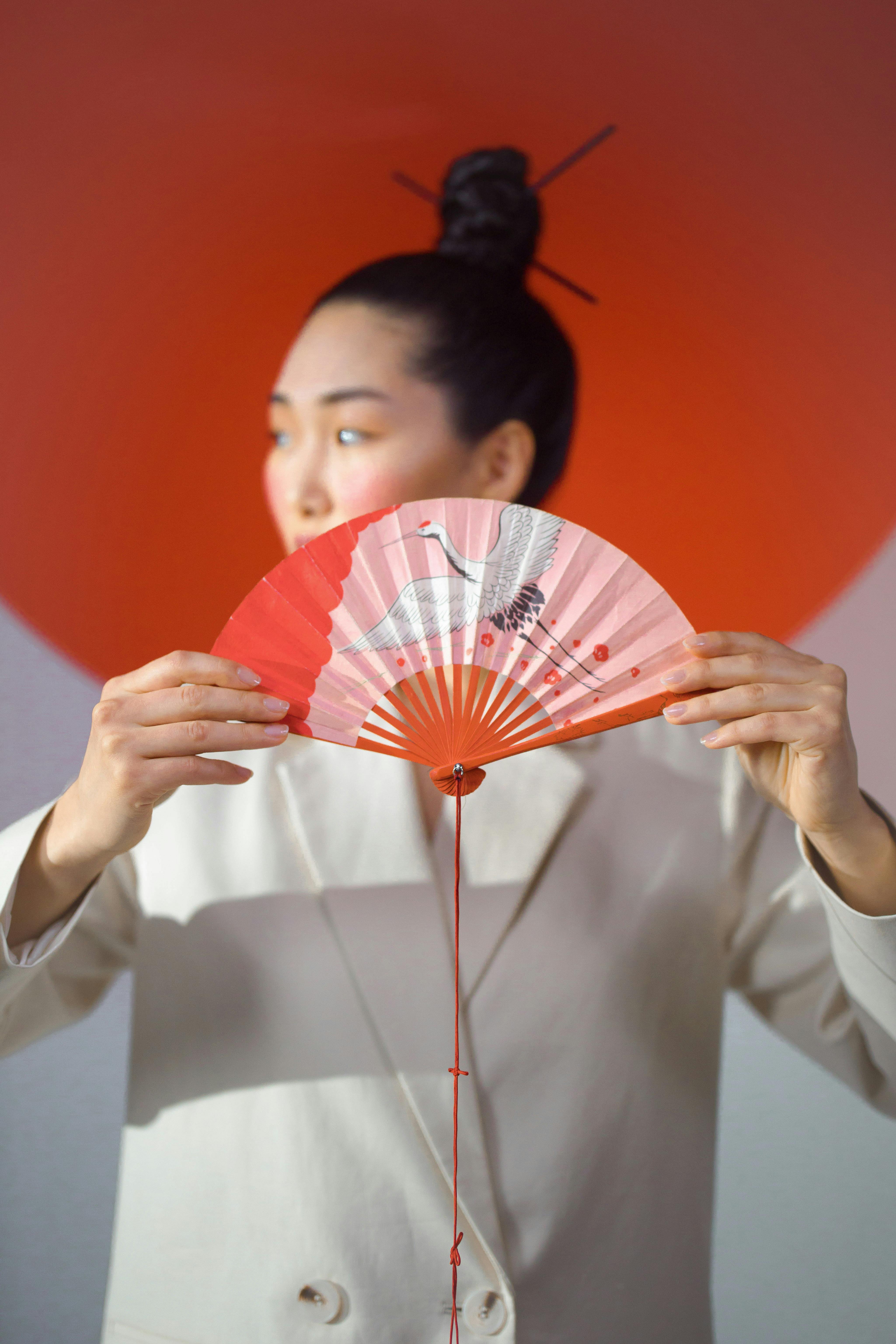 Portrait of a woman in a suit holding a decorative Japanese fan, with a conceptual and minimalist style.