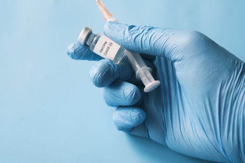 Free Blue gloved hand holding a COVID-19 vaccine vial and syringe on a blue background. Stock Photo