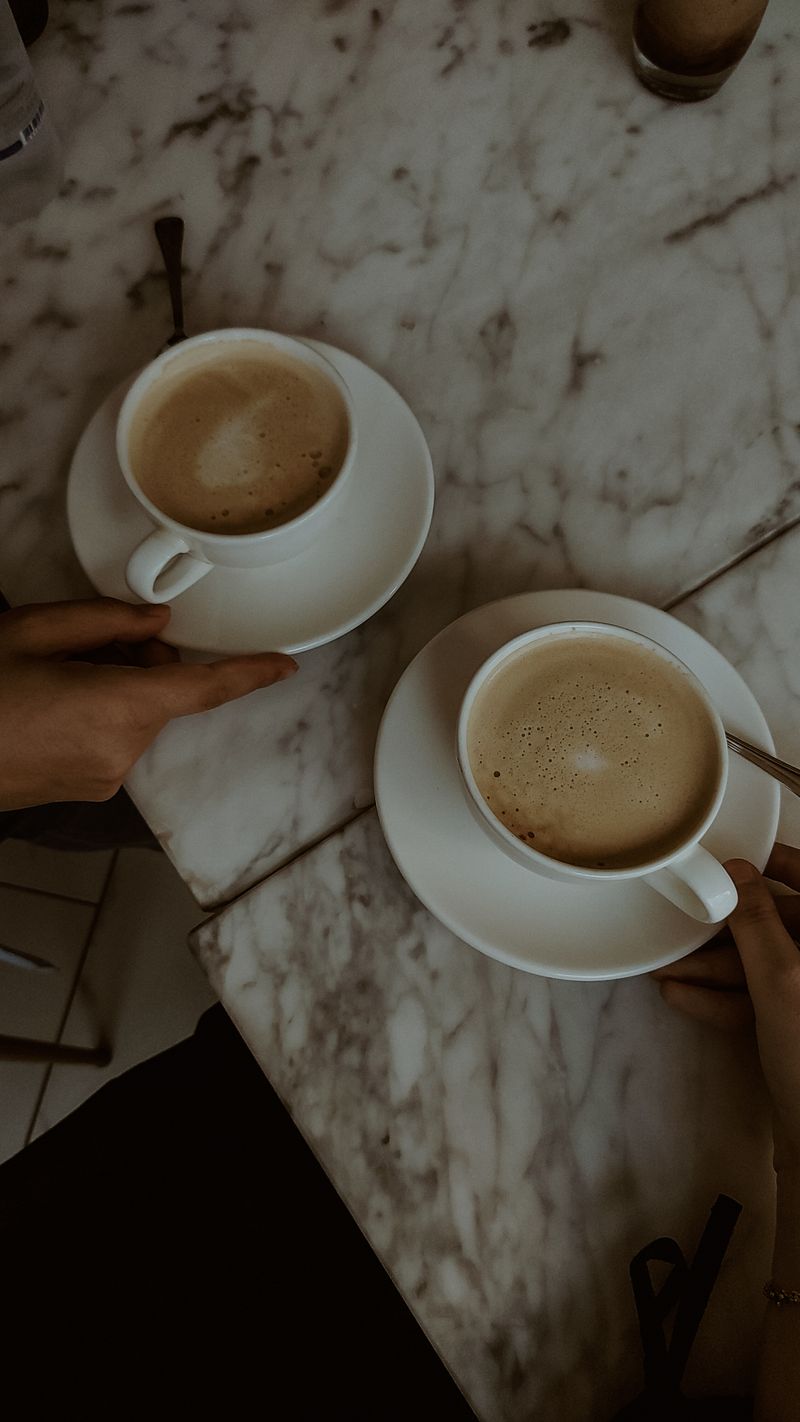 Two coffee cups held together over a marble table