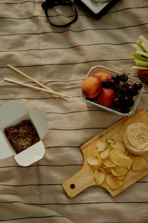 Free Top view of a picnic setup with Asian takeaway, fresh fruits, and a variety of snacks. Stock Photo