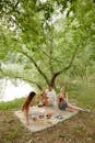 3 Women Sitting on Ground Near Body of Water