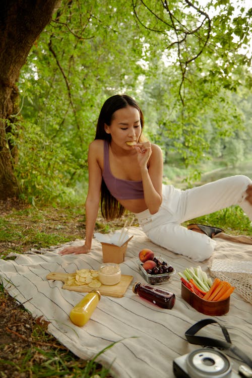 Free Woman Eating While Sitting on a Picnic Blanket Stock Photo
