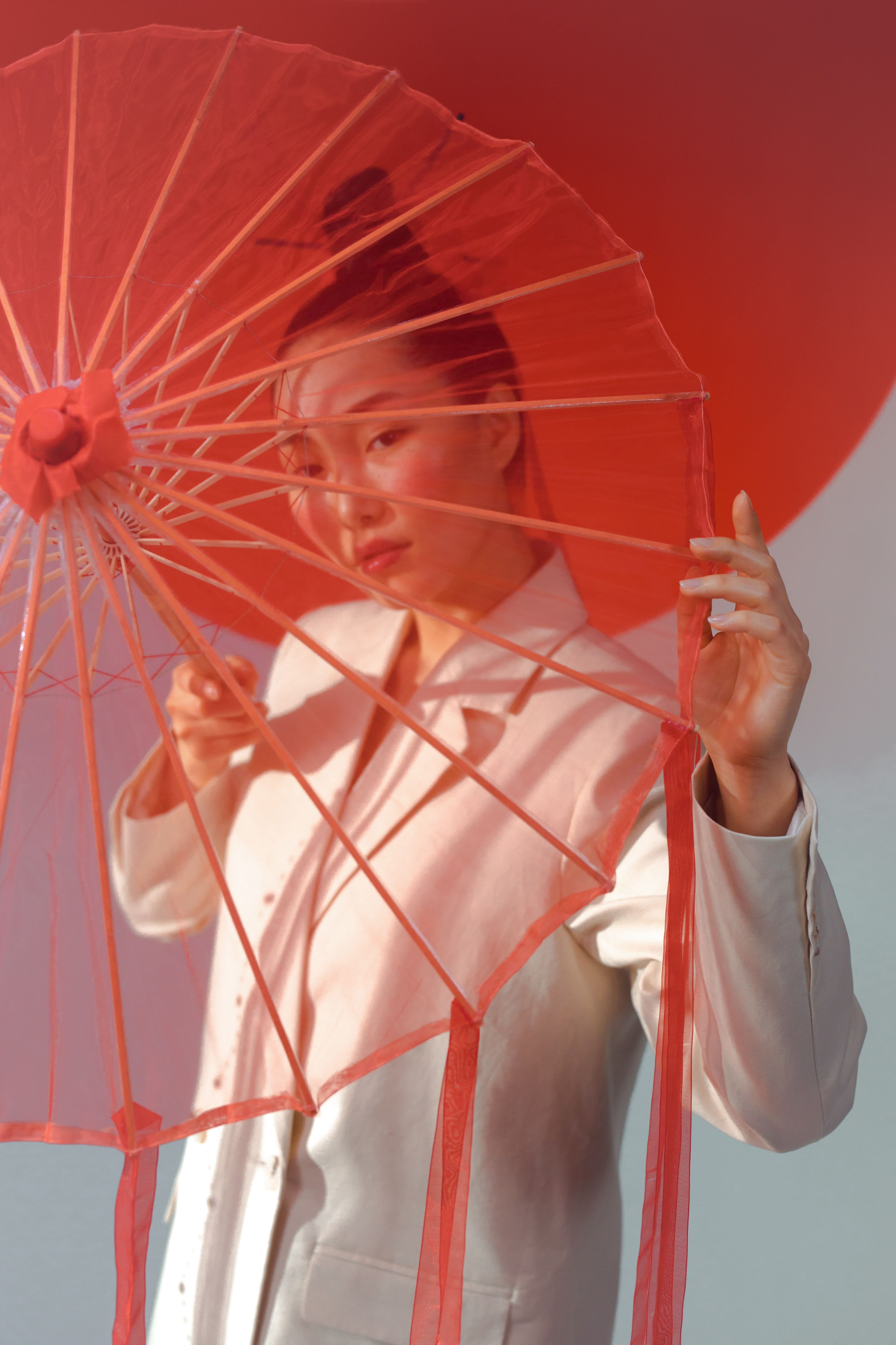 Portrait of an Asian woman in white, posing with a red umbrella, exuding elegance and style.