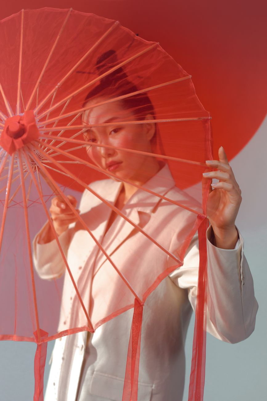 Portrait of an Asian woman in white, posing with a red umbrella, exuding elegance and style.