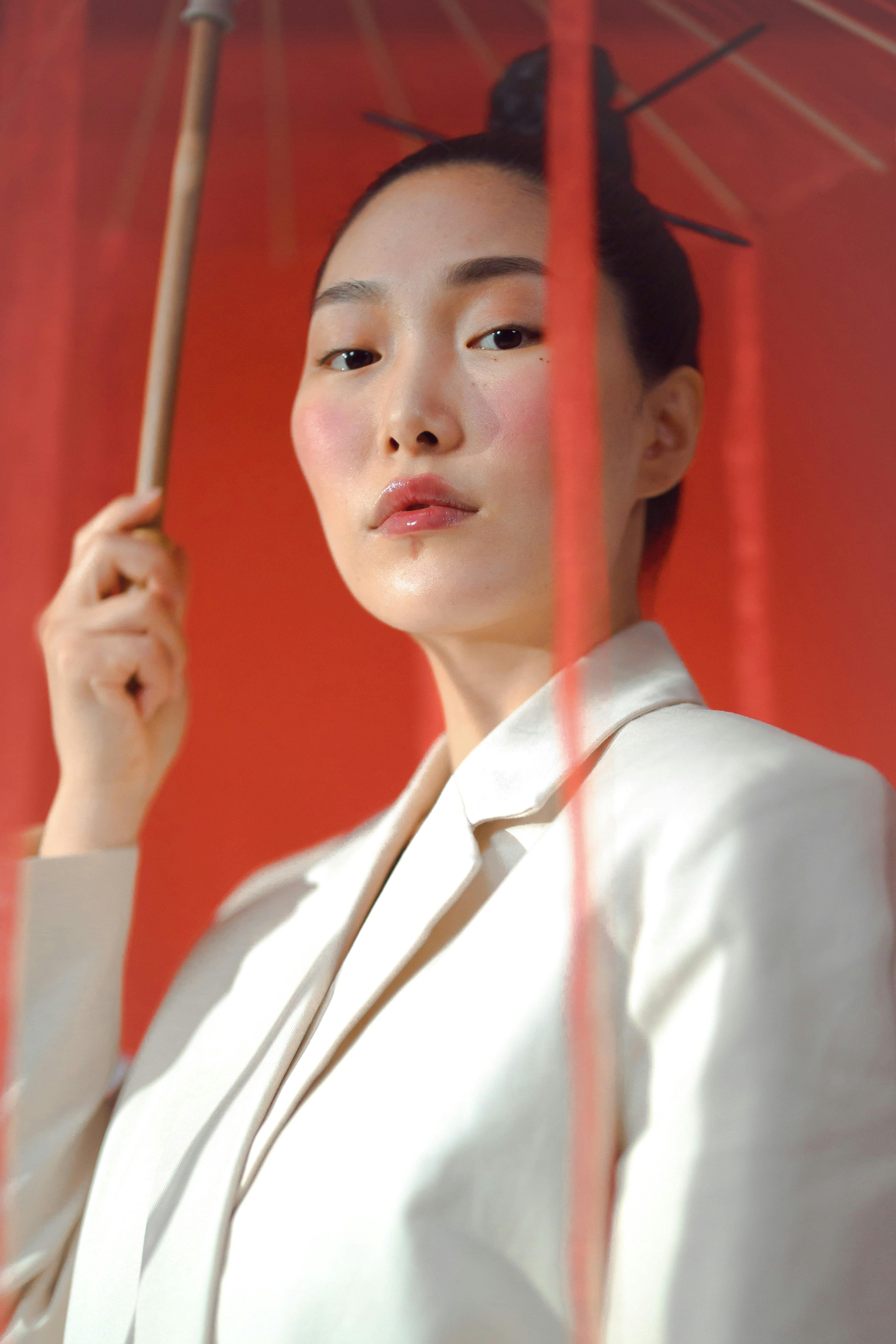 woman in white blazer holding red wagasa while seriously looking at the camera