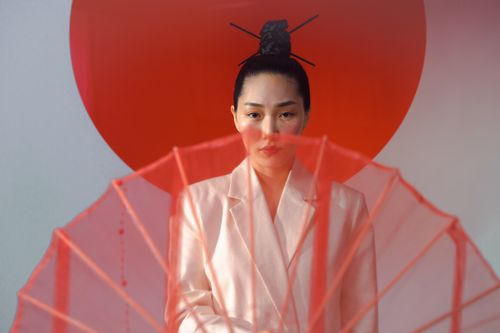 Free Stylish portrait of an Asian woman in a white blazer with a traditional hair bun and red umbrella. Stock Photo