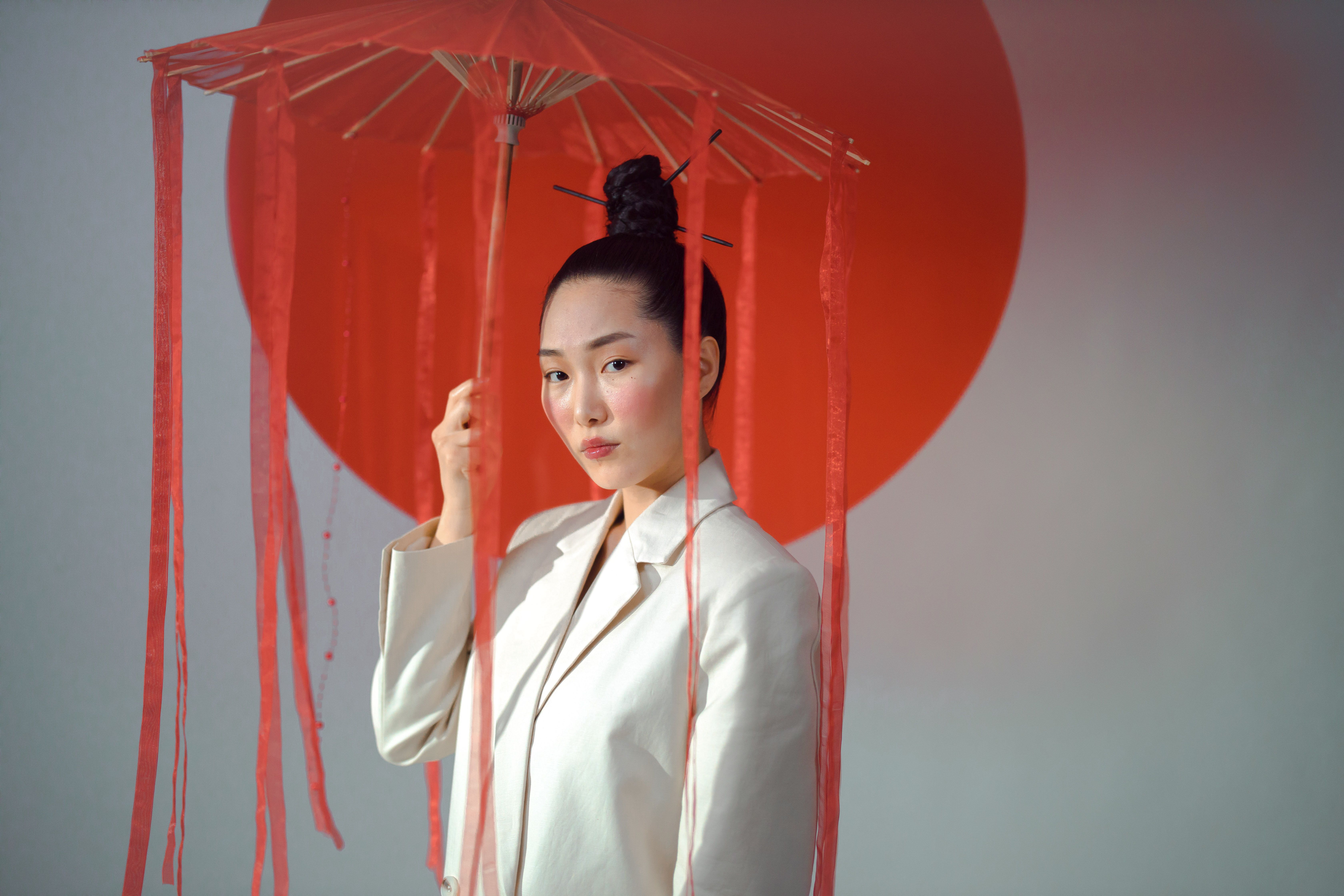 Portrait of an Asian woman in a white blazer, holding a red umbrella, showcasing elegance and cultural fusion.