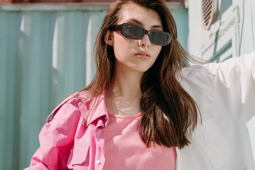Stylish woman wearing sunglasses and pink outfit, standing outdoors with modern vibe.