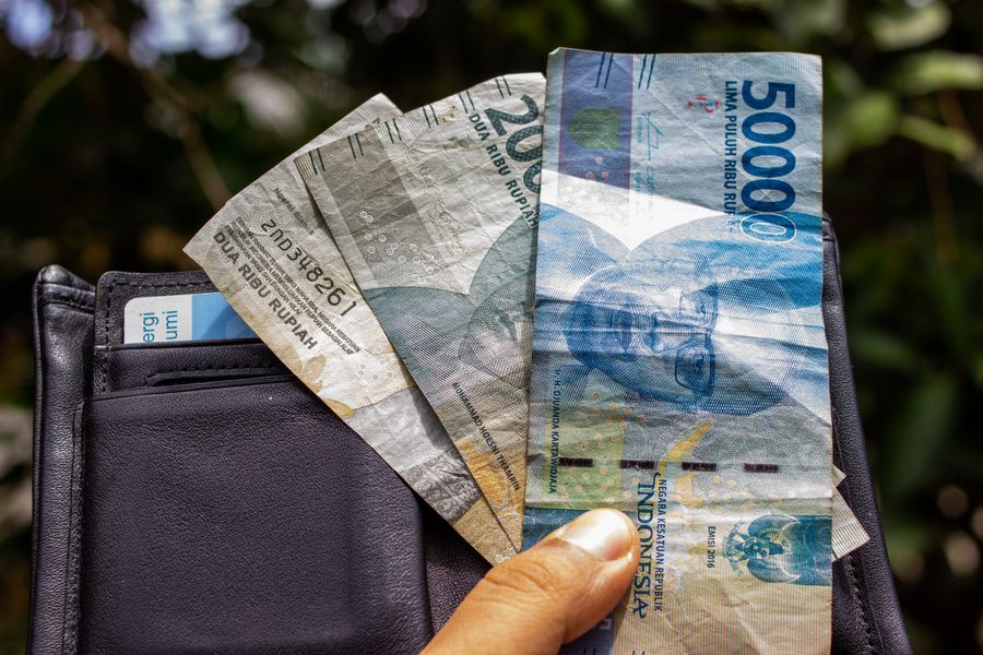 Close-up of a hand holding Indonesian Rupiah banknotes outdoors with a wallet.