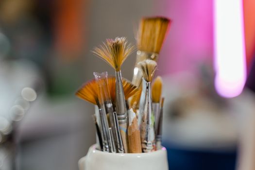 Artistic paintbrushes in a holder with a blurred colorful background.