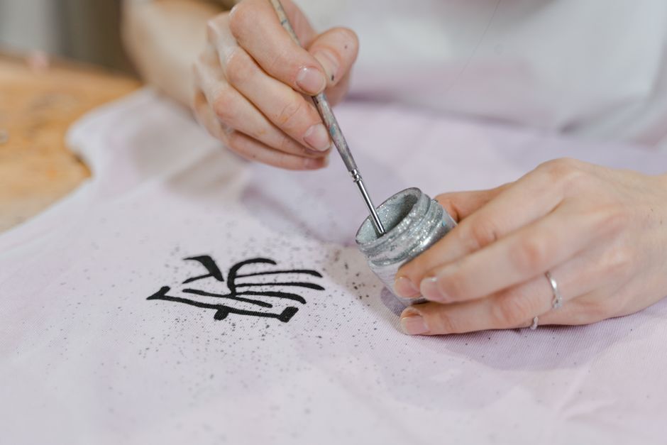 Close-up of an artisan hand painting textile with glitter and brush.