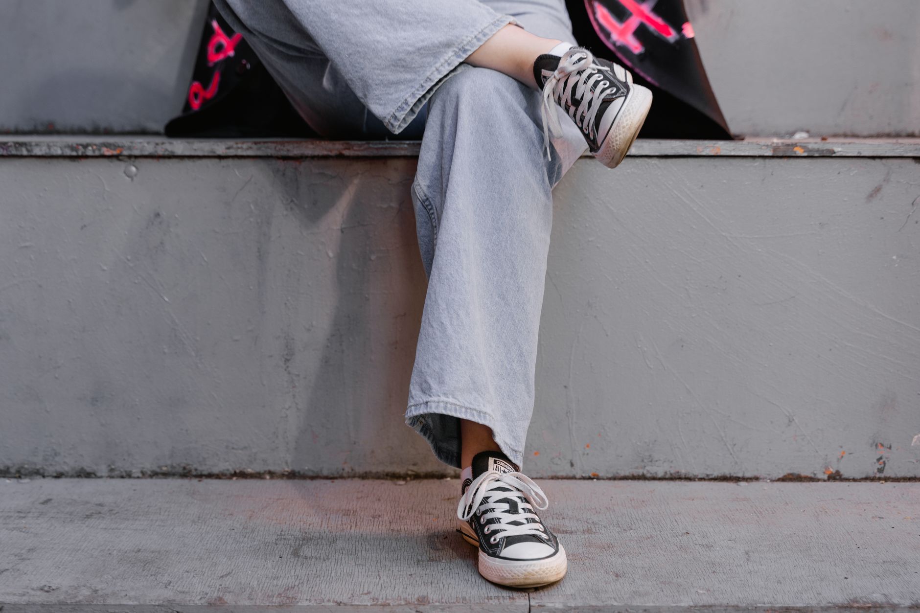 Candid shot of crossed legs wearing black sneakers and denim, sitting on a concrete step.