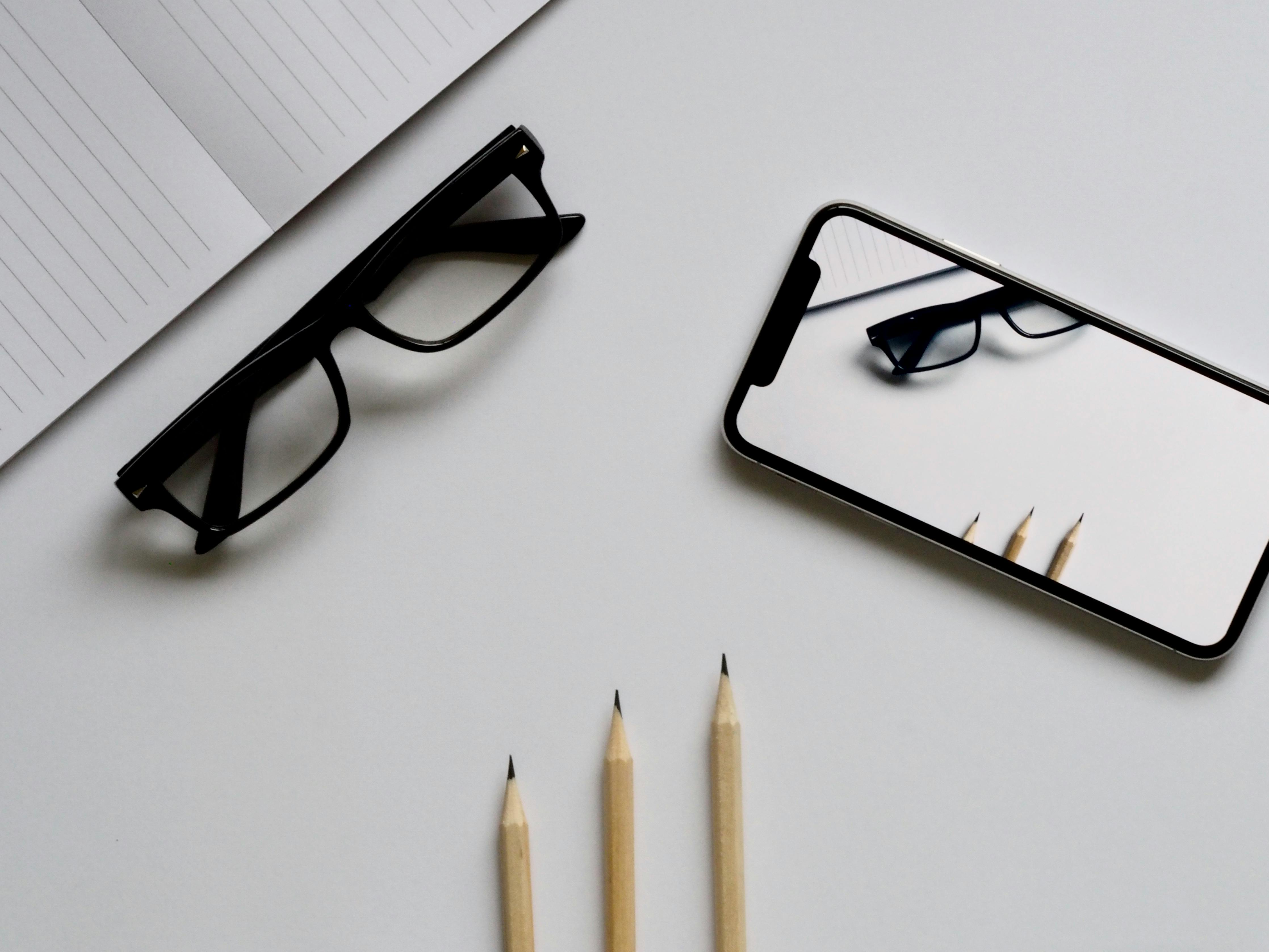 three pencils eyeglasses and smartphone on white table