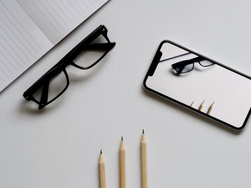 Free Three Pencils, Eyeglasses, and Smartphone on White Table Stock Photo