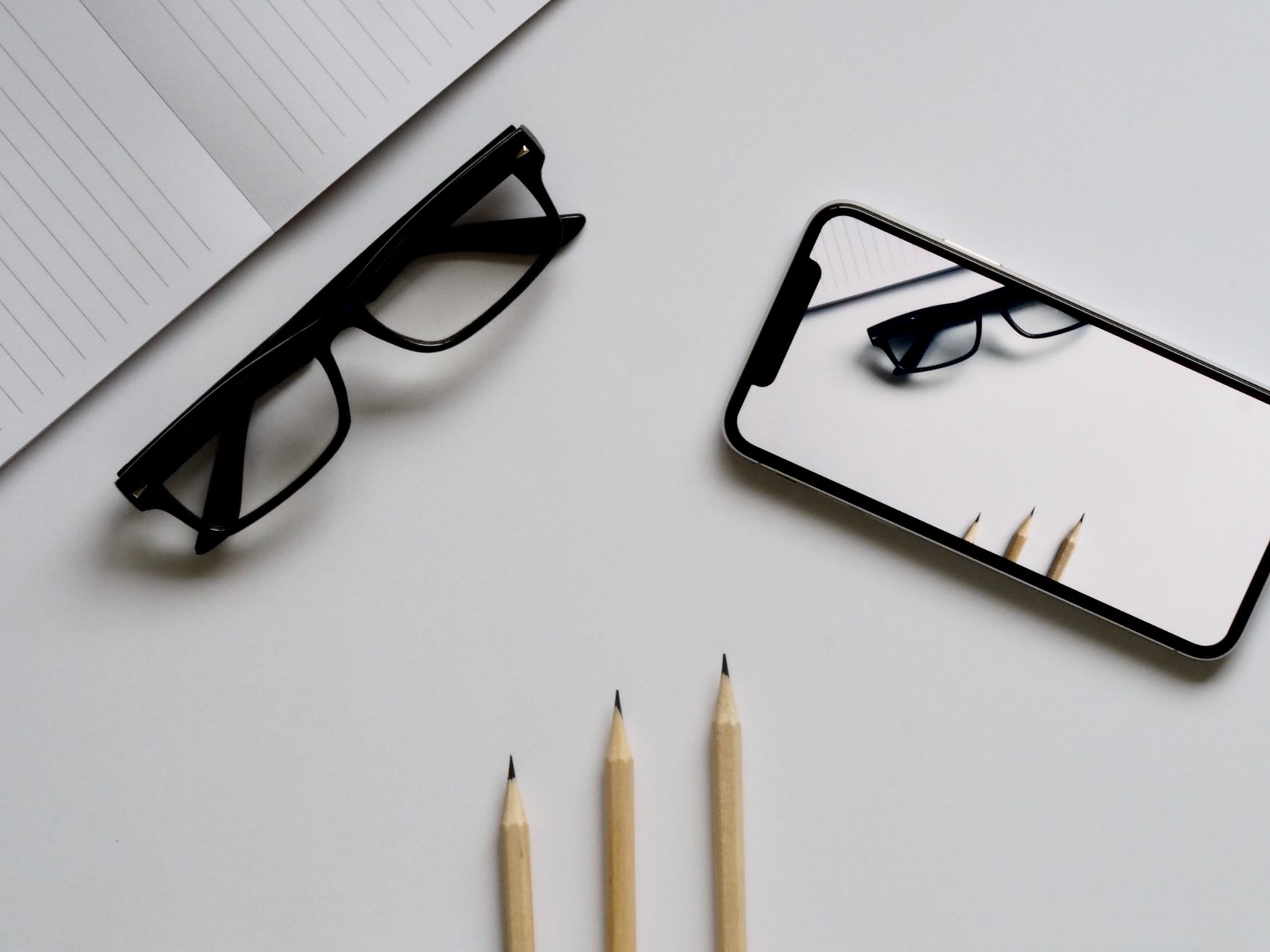Stylish minimalist flat lay with smartphone reflection of glasses and pencils on white background.