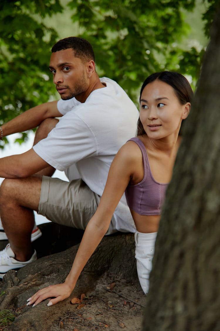 Young Man And Woman Sitting On A Tree In A Park 