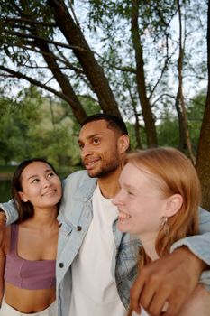 Three friends smiling together in an outdoor setting, showcasing diversity and friendship.