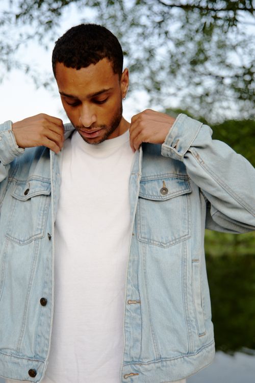 Free Stylish man adjusting denim jacket in a serene outdoor setting. Stock Photo